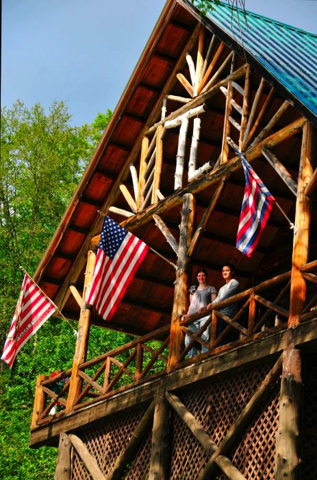 Two individuals gaze down from the balcony of a log cabin.