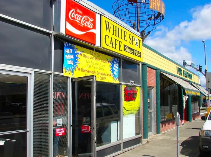 A series of building facades with dark windows. Above one entrance, bright signs stand out, including a yellow one for Bright Spot Cafe and a red Coca-Cola sign.