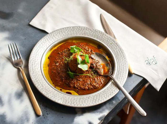 A hearty bowl of stew featuring a large meatball at its center, presented on a slate table with an elegant setting.