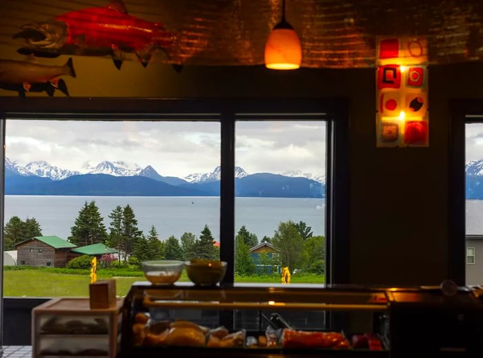 A dining room window offers a stunning view of mountains and a serene lake in the background.