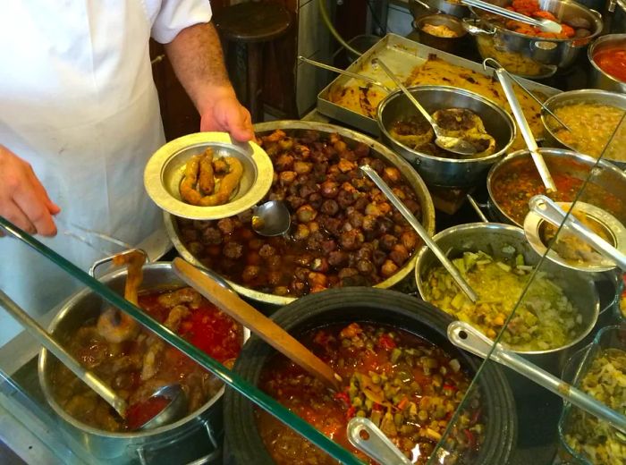 A chef serves a variety of stews and dishes onto a plate.