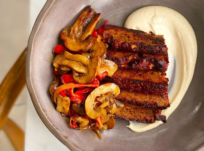 Aerial view of a plate featuring seitan strips, a drizzle of cream, and roasted vegetables.