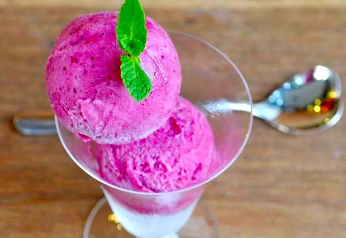 A vibrant scoop of purple ice cream served in a bowl, garnished with a sprig of mint.