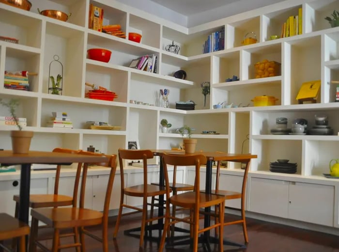 A dining space adorned with large white built-in shelves that display an array of colorful cookware.