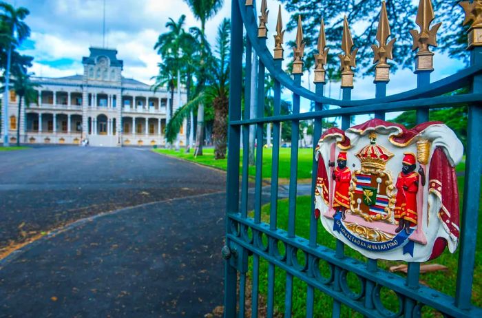 An ornate crest on the gate leading to a majestic palace, surrounded by swaying palm trees.