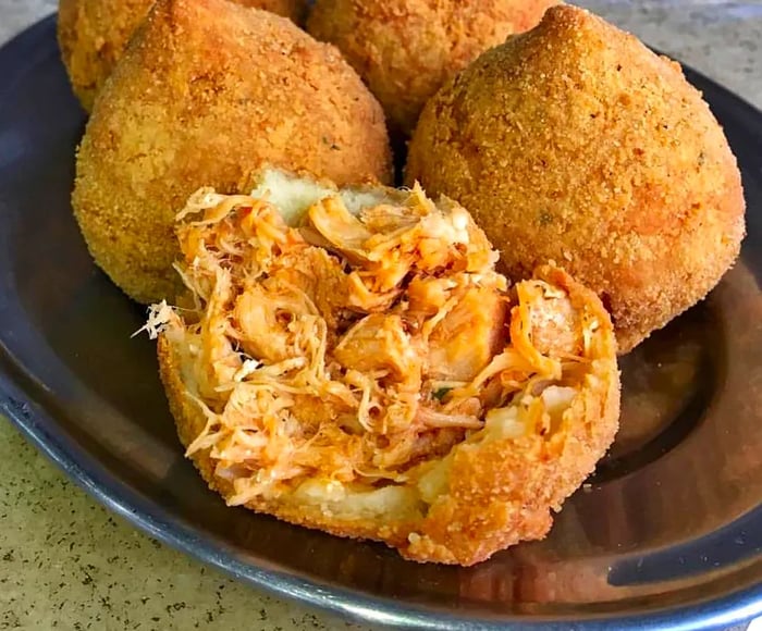 A plate featuring several coxinhas, with one at the front opened to show the chicken filling inside.