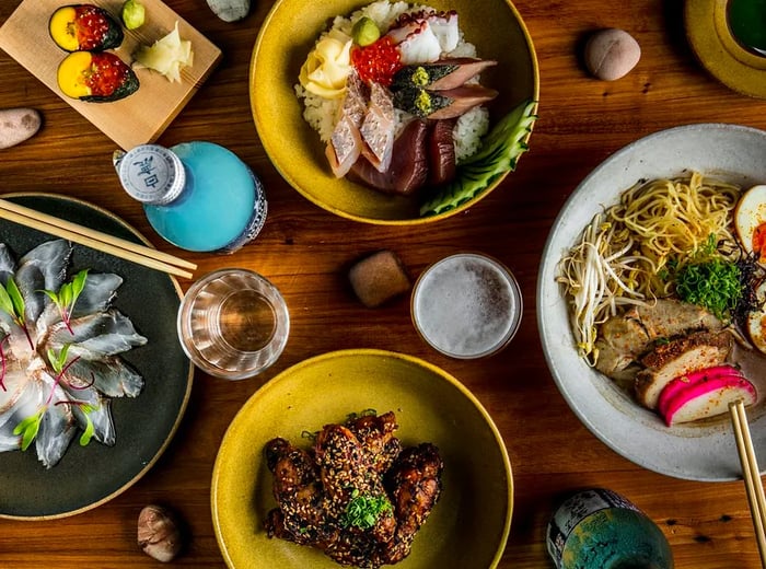 An overhead view of a platter featuring ramen, spicy chicken wings, and fresh crudo.