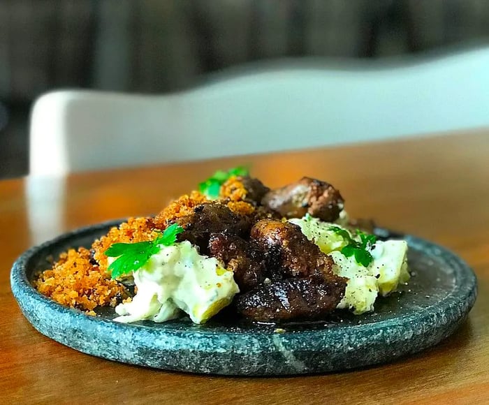 A broad, low-rimmed dark marble plate adorned with chicken, generous servings of potato salad, and rice, all garnished with fresh herbs.