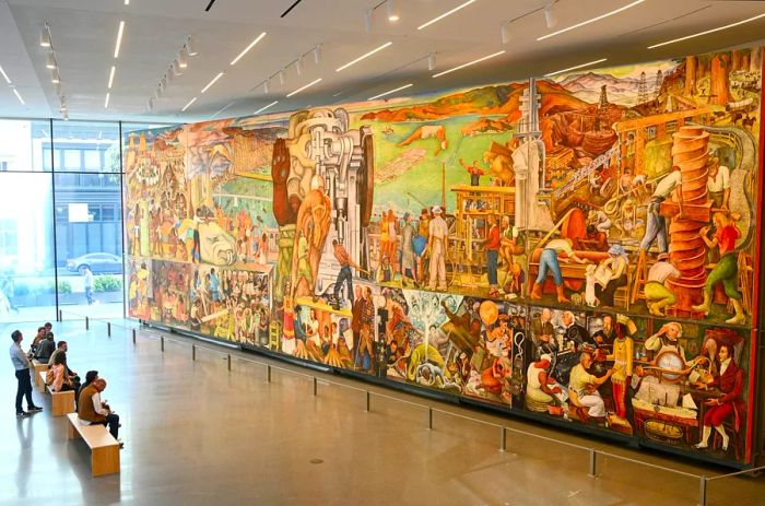 Visitors relax on a bench in a spacious gallery, admiring a mural that spans an entire wall