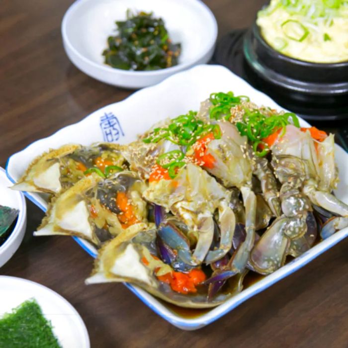 Cooked crabs arranged on a plate, garnished with scallions and sesame seeds.