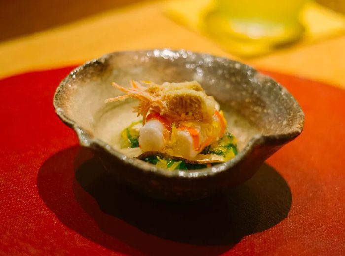 Raw shrimp elegantly presented on a clam shell, adorned with fried shrimp heads and accompanied by a variety of other ingredients.