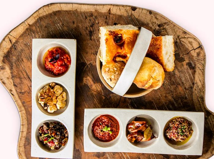 A bird's-eye view of an assortment of breads, dips, and small bites artfully arranged on a large wooden platter.