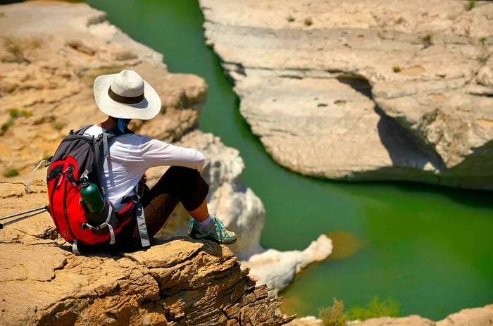 A scenic view from behind a hat-clad hiker gazing down at Wadi Daykha, Oman