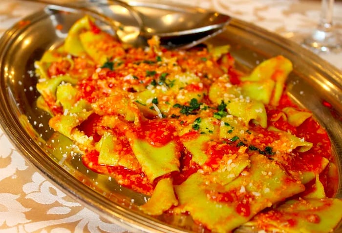 A long silver platter holds pasta topped with grated cheese, fresh tomato sauce, and herbs.