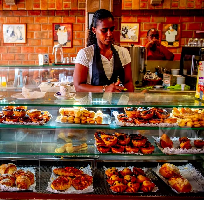 A staff member behind the pastry display, with a customer observing from across the counter.