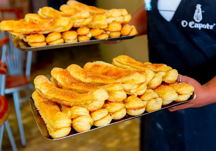 A baker carries trays filled with rows of pastries.