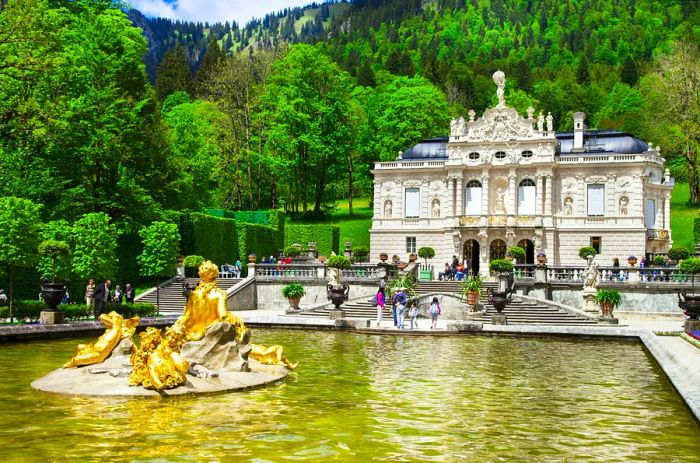 Visitors enjoy the scenery by the water at Linderhof Palace during summer, with the Alps in the backdrop, Bavaria