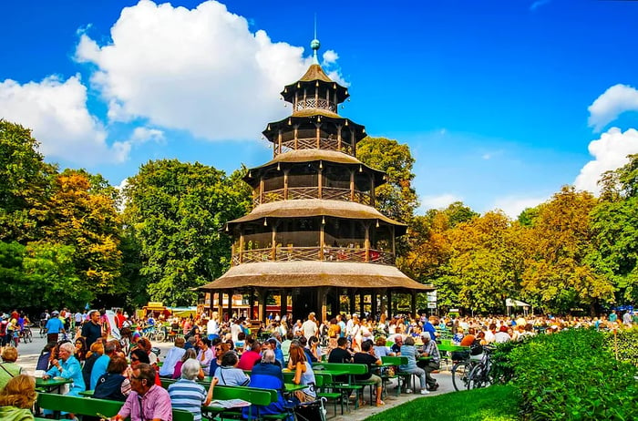 On a sunny day, visitors enjoy drinks at tables in the biergarten near the Chinese Tower in Munich’s Englischer Garten.