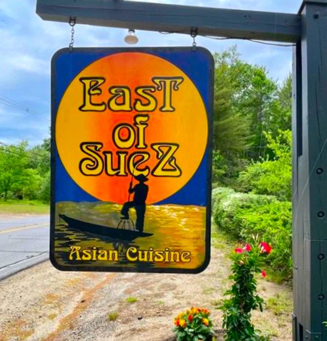 A sign reading East of Suez and Asian Cuisine, featuring a lone boat operator under the night sky.