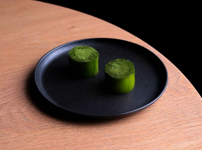 Cylinders of pickled cucumber arranged on a dark plate, garnished with a delicate green topping.