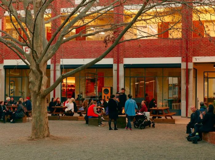 Guests mingle at tables in a courtyard under the shade of a large tree.