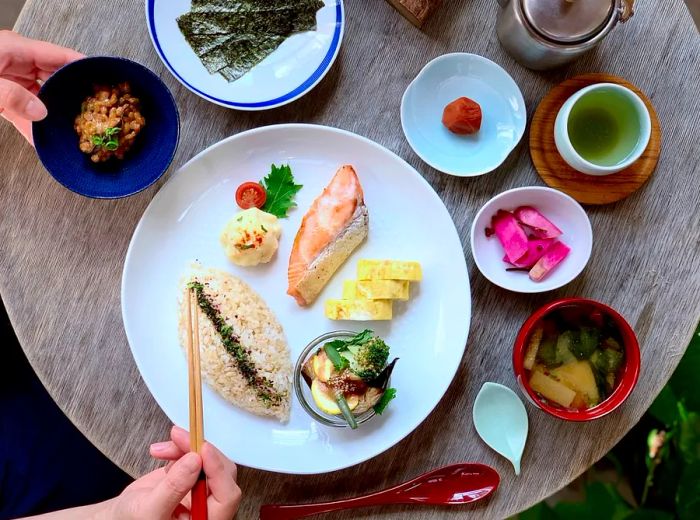 From above, a beautifully arranged plate of fish, rice, and an assortment of sides sits on a wooden table.