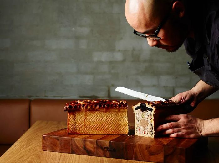 A chef carefully slices a large piece of pate en croute with a knife.