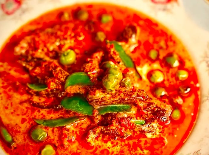 A close-up view of a bowl filled with curry and scattered peas.