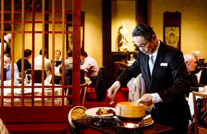 A waiter presents a dish at the table at Flower Drum