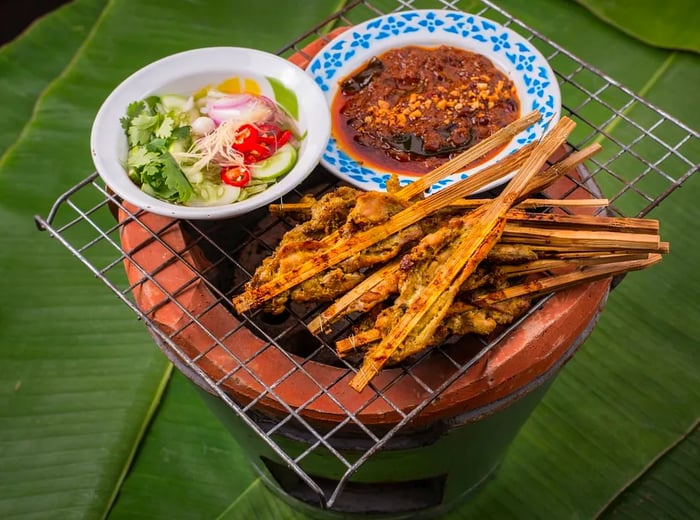 Grilled meat skewers served on a grate alongside a variety of sauces and chopped garnishes.