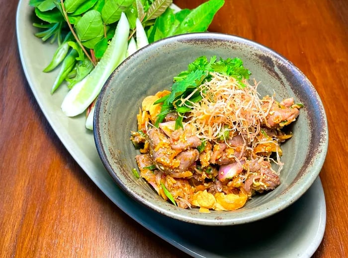 A dish of duck larb topped with a heap of crispy garnishes, elegantly arranged on a long platter alongside fresh greens.