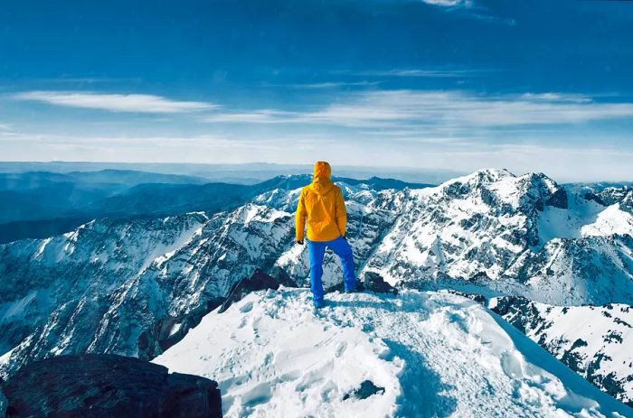 A hiker gazes at the snow-covered peaks of the High Atlas Mountains from the summit of Mt Toubkal, Morocco