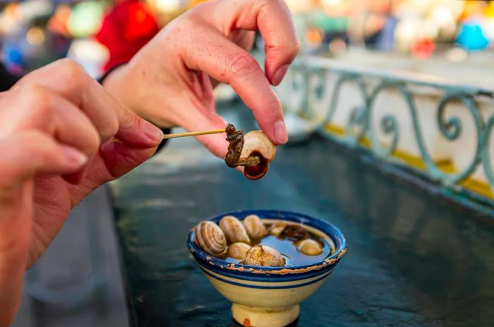 A woman carefully removes a snail from its shell in a bowl of soup in Morocco.