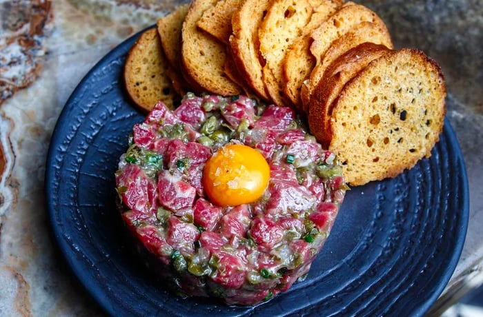 A hearty serving of steak tartare garnished with a raw egg yolk, accompanied by slices of toast.