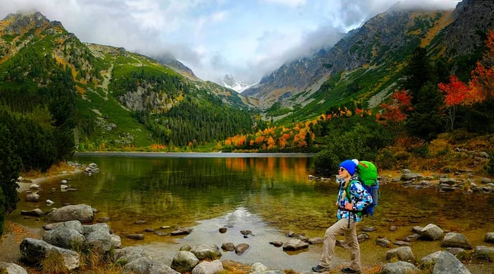 A young hiker enjoys the vibrant autumn scenery near Popradske Pleso lake in the High Tatras, surrounded by colorful mountains.