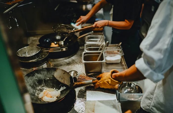 Chefs in the kitchen, with one cooking an egg in a wok.