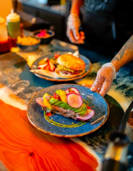 A chef presents a beautifully layered avocado toast from behind the counter.