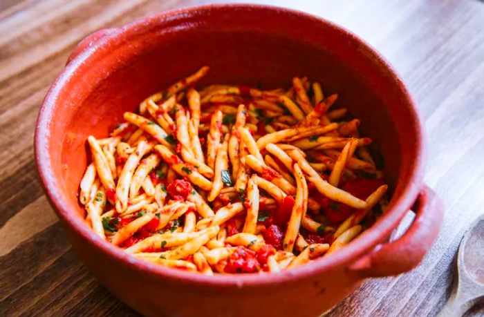 A large earthenware pot filled with pasta in a rich red sauce.