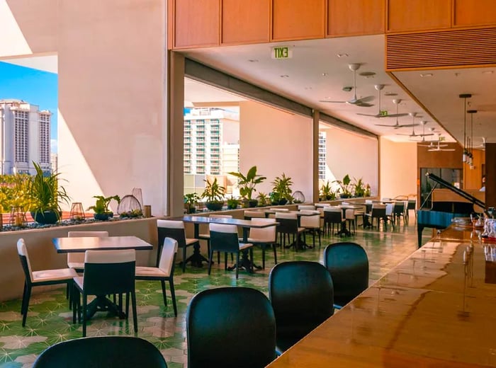 A spacious dining area with empty bar stools, showcasing tables along a wall with wide-open windows.