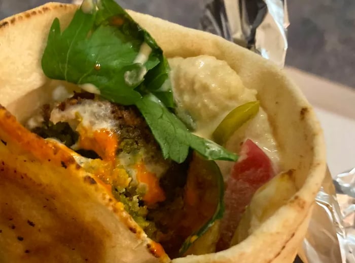 A close-up view of a falafel wrap filled with vegetables and sauces.