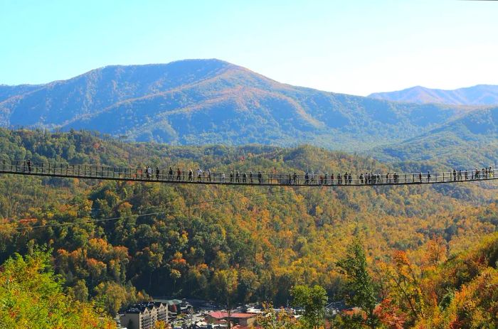 Visitors stroll across the SkyBridge in Gatlinburg, framed by mountains and autumn foliage.