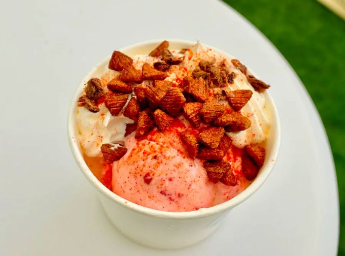 A cup filled with various ice cream flavors topped with crunchy bits, set on a white outdoor table.