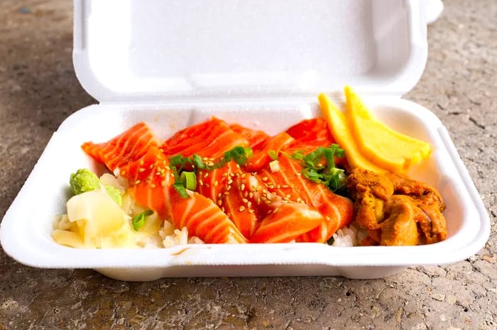 A takeout box filled with slices of salmon sashimi, scallions, pickled ginger, and uni.