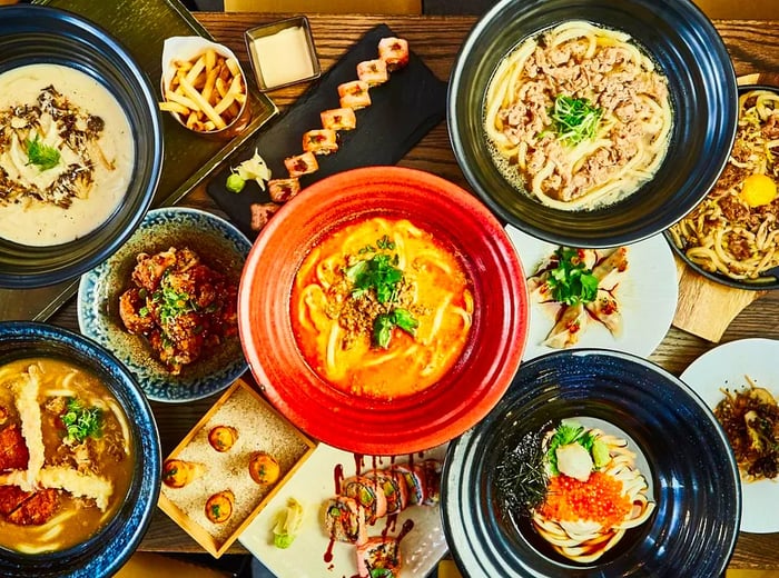 A table brimming with an array of dishes, featuring various noodle soups, maki rolls, gyoza, and uni starters.