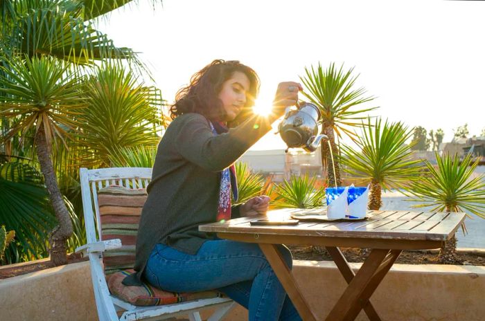 A woman pours tea into cups on a patio in Morocco.