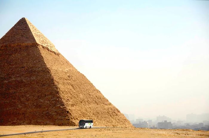 A bus passes by a grand stone pyramid in a dusty landscape.