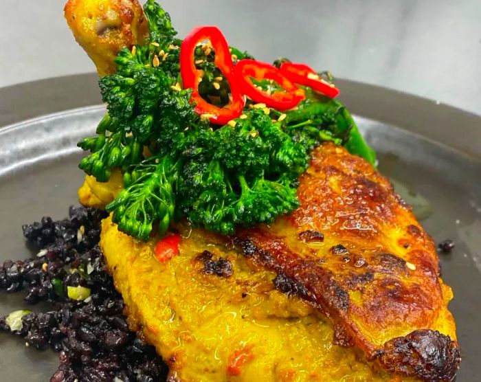 A generous serving of chicken resting on a bed of flavorful rice, topped with sunflower seeds and broccolini