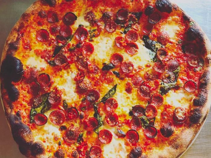 An overhead view of a complete pizza topped with pepperonis and basil.