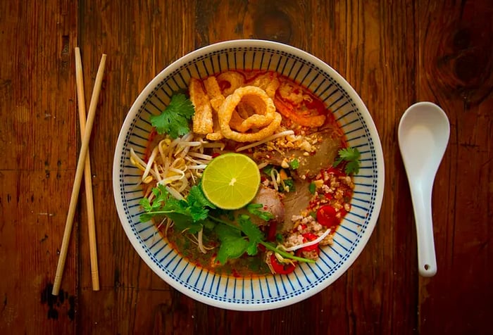 An aerial view of a bowl of noodle soup, accompanied by chopsticks and a soup spoon.