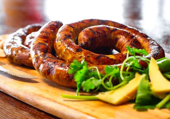 Sausage rolls on a cutting board accompanied by cheese and herbs